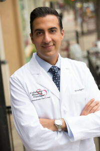 Male doctor in white coat poses for a headshot outside